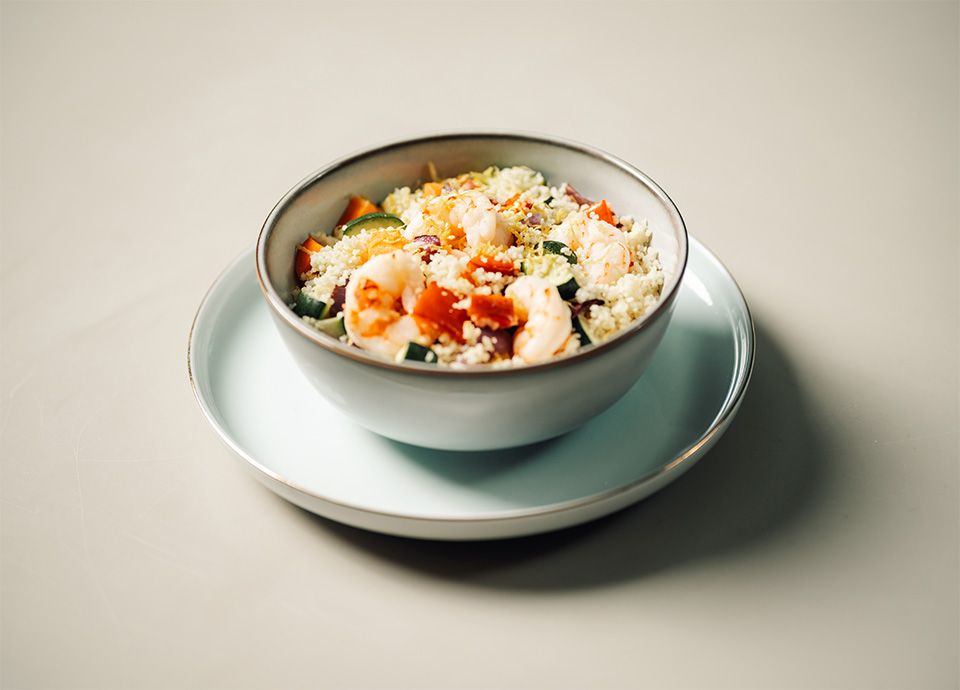 Couscous con gamberi e verdure colorate servito su un piatto di ceramica color crema