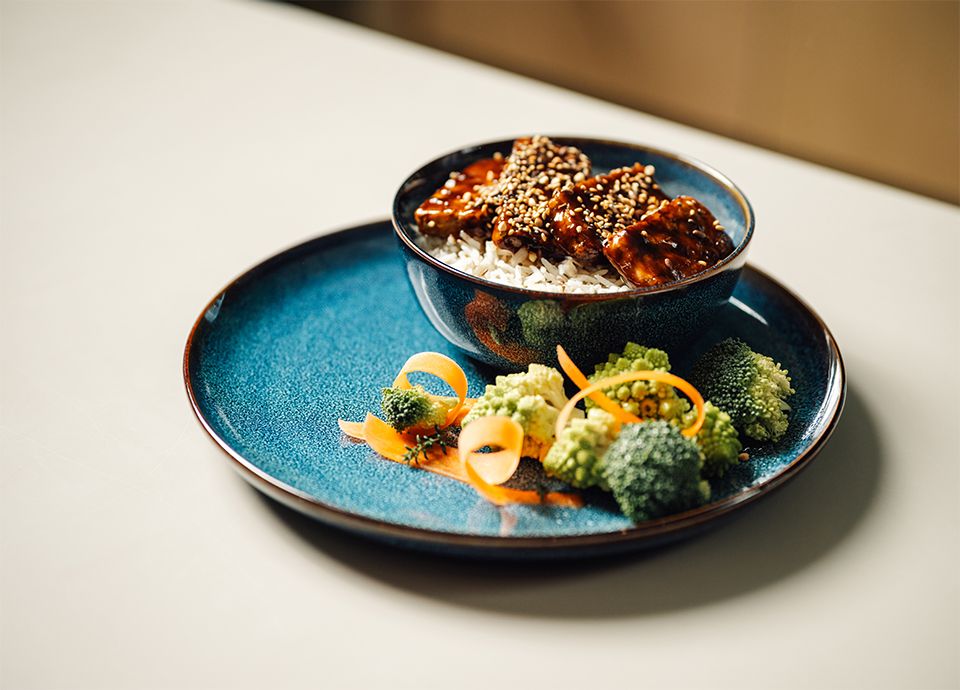Tofu teriyaki servito con semi di sesamo e verdure su un piatto di ceramica azzurro