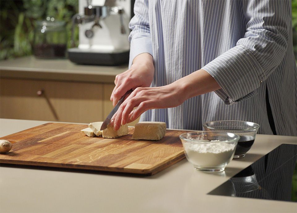 Persona che taglia il tofu a pezzi su un tagliere