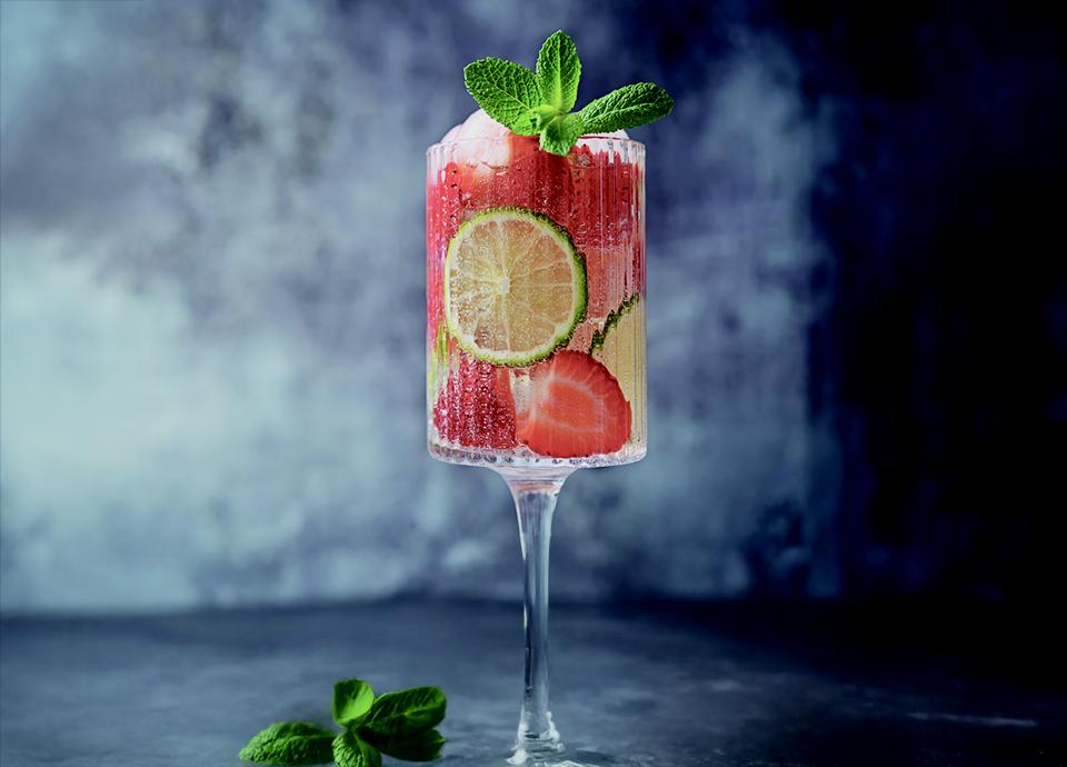 Bicchiere alto con cocktail, fragole, fette di lime e menta.